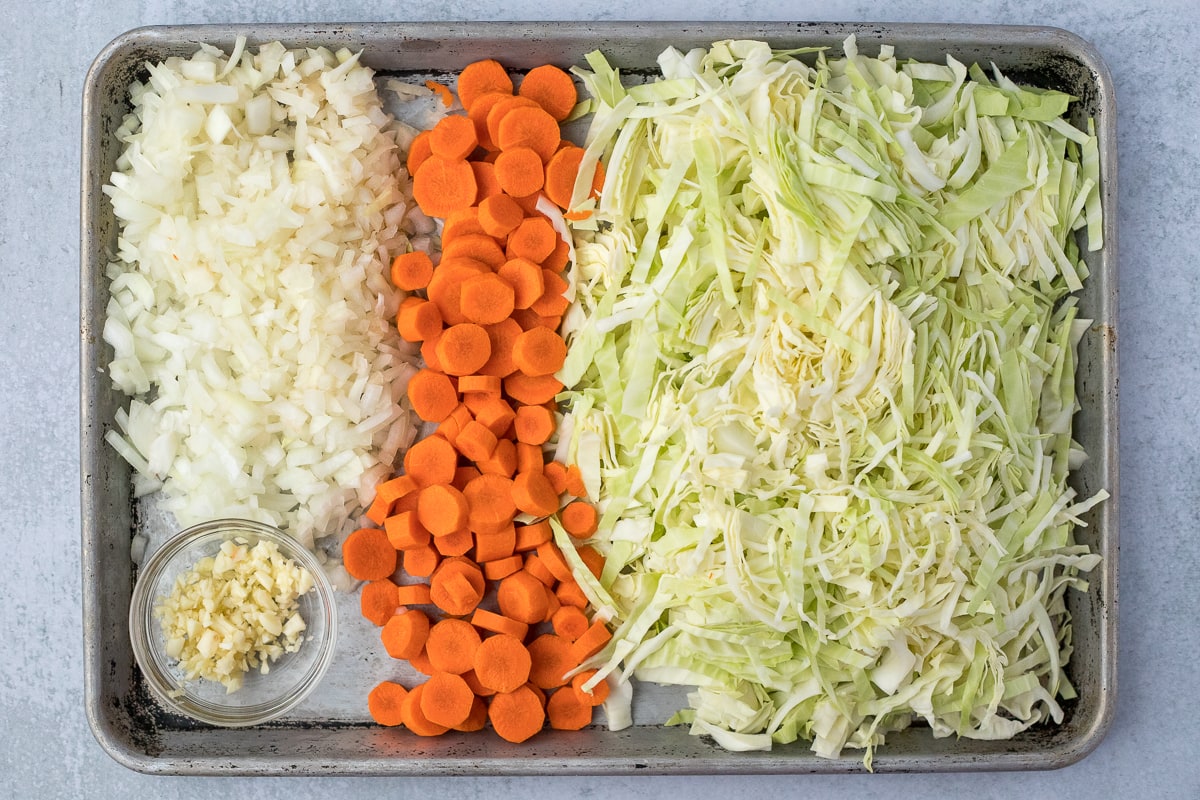 baking sheet with shredded cabbage, diced carrots, cut onion and garlic