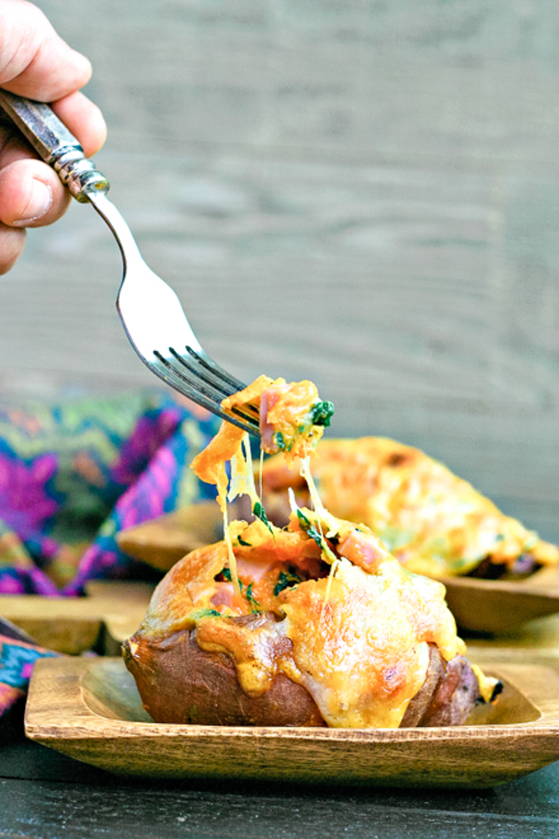 using a fork to dig into melted cheese on a stuffed sweet potato