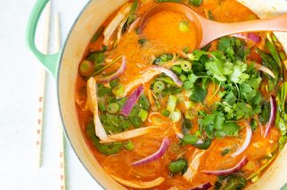 large pot of thai red curry soup with serving spoon and greens on top