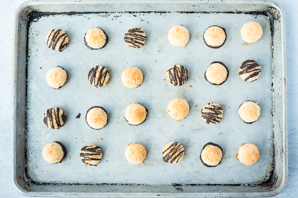 baking sheet with baked coconut macaroons, some topped with drizzled chocolate and some plain