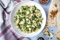 white bowl of marinated gigantes beans with pita bread on the side