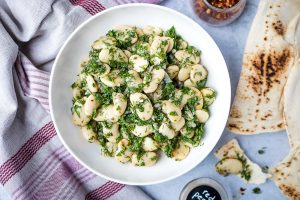 white bowl of marinated gigantes beans with pita bread on the side