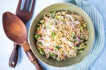 large serving bowl of peanut noodles with chicken next to oversized wood serving spoons