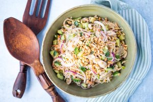 large serving bowl of peanut noodles with chicken next to oversized wood serving spoons