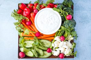 wood platter of fresh vegetables with white bowl of ranch dip