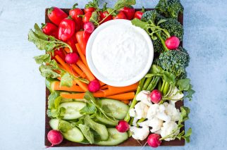 wood platter of fresh vegetables with white bowl of ranch dip