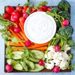 close up of square platter of cut vegetables with round bowl of miso ranch dip in center
