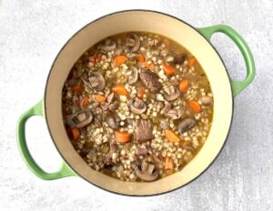 dutch oven with cooked beef barley soup with mushrooms